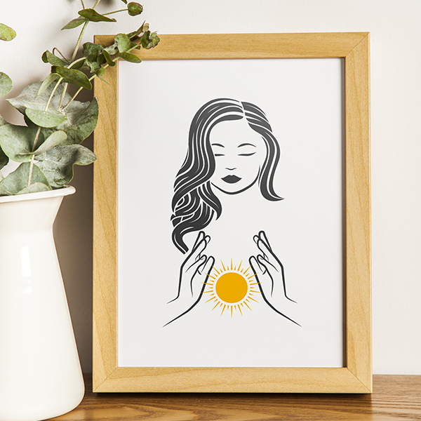 Gravure encadrée d'un visage féminin et de mains en coupe autour d'un symbole solaire, tons bois et papier près d'une plante verte